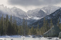 A frozen lake surface in the foreground with snow-covered peaks and spires of the Continental Divide behind