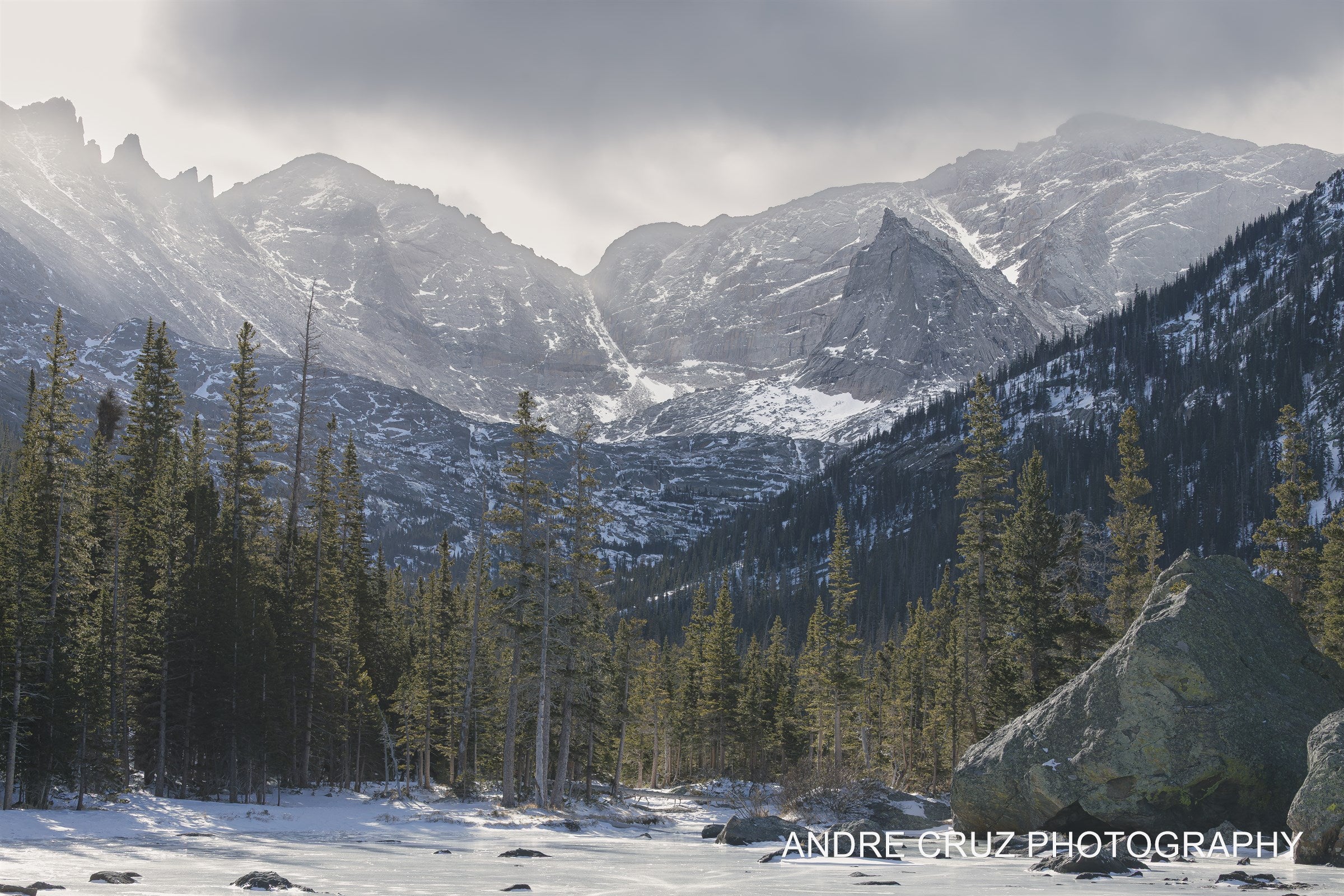 A frozen lake surface in the foreground with snow-covered peaks and spires of the Continental Divide behind