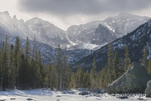 A frozen lake surface in the foreground with snow-covered peaks and spires of the Continental Divide behind