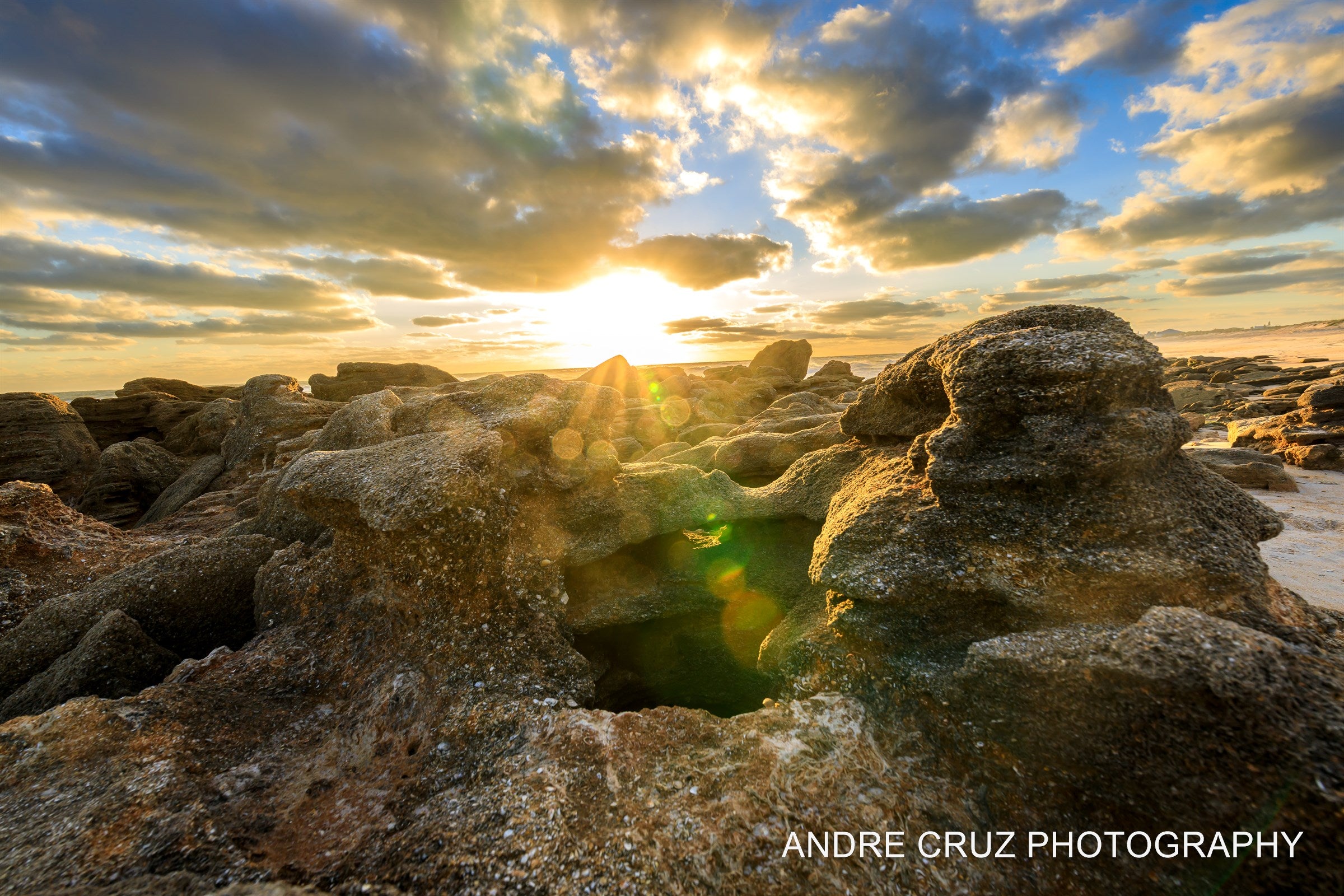 Sunburst breaking over weathered coquina rock formations at dawn, Florida coast