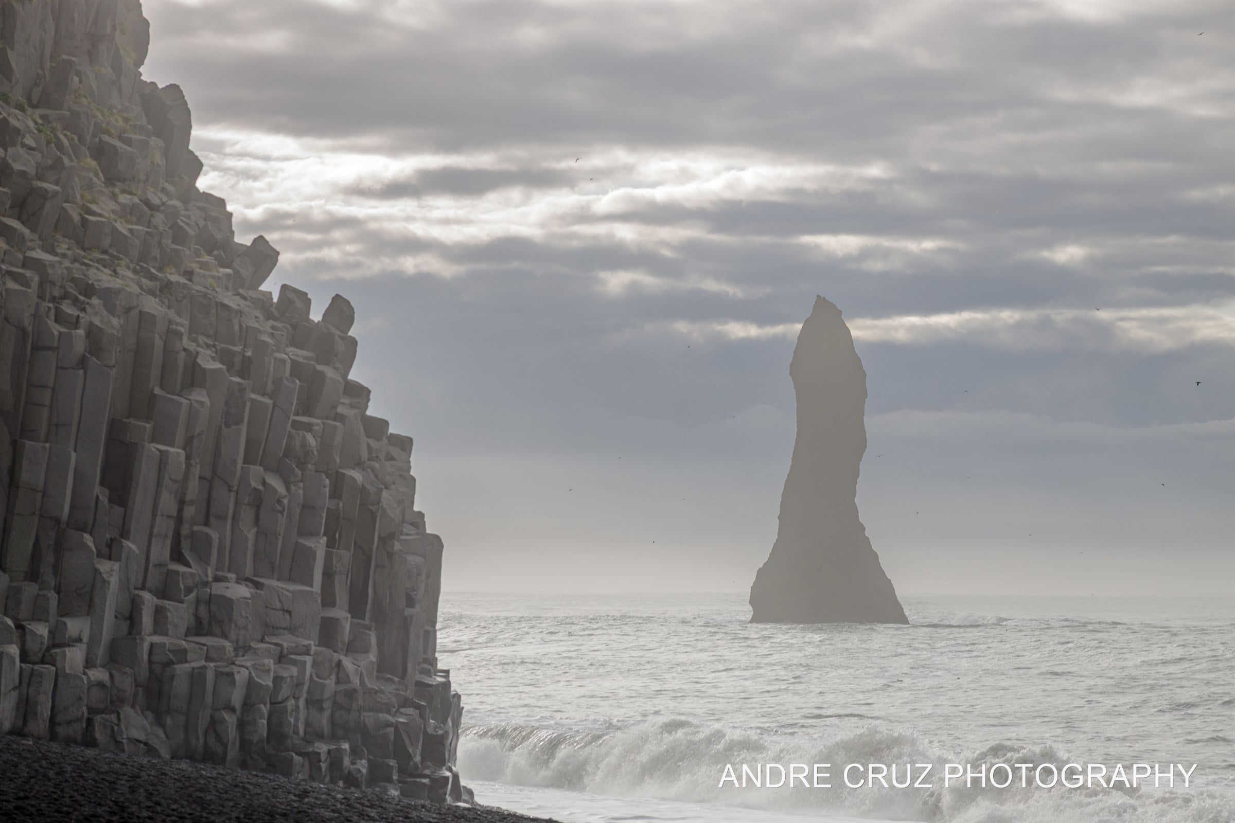 Basalt columns at Reynisfjara with a sea stack rising from the surf in mist, Iceland