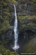 A tall thin waterfall dropping into a moss-covered basalt canyon in southern Iceland