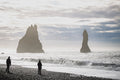 The Reynisdrangar sea stacks off a black sand beach with two figures for scale, Iceland