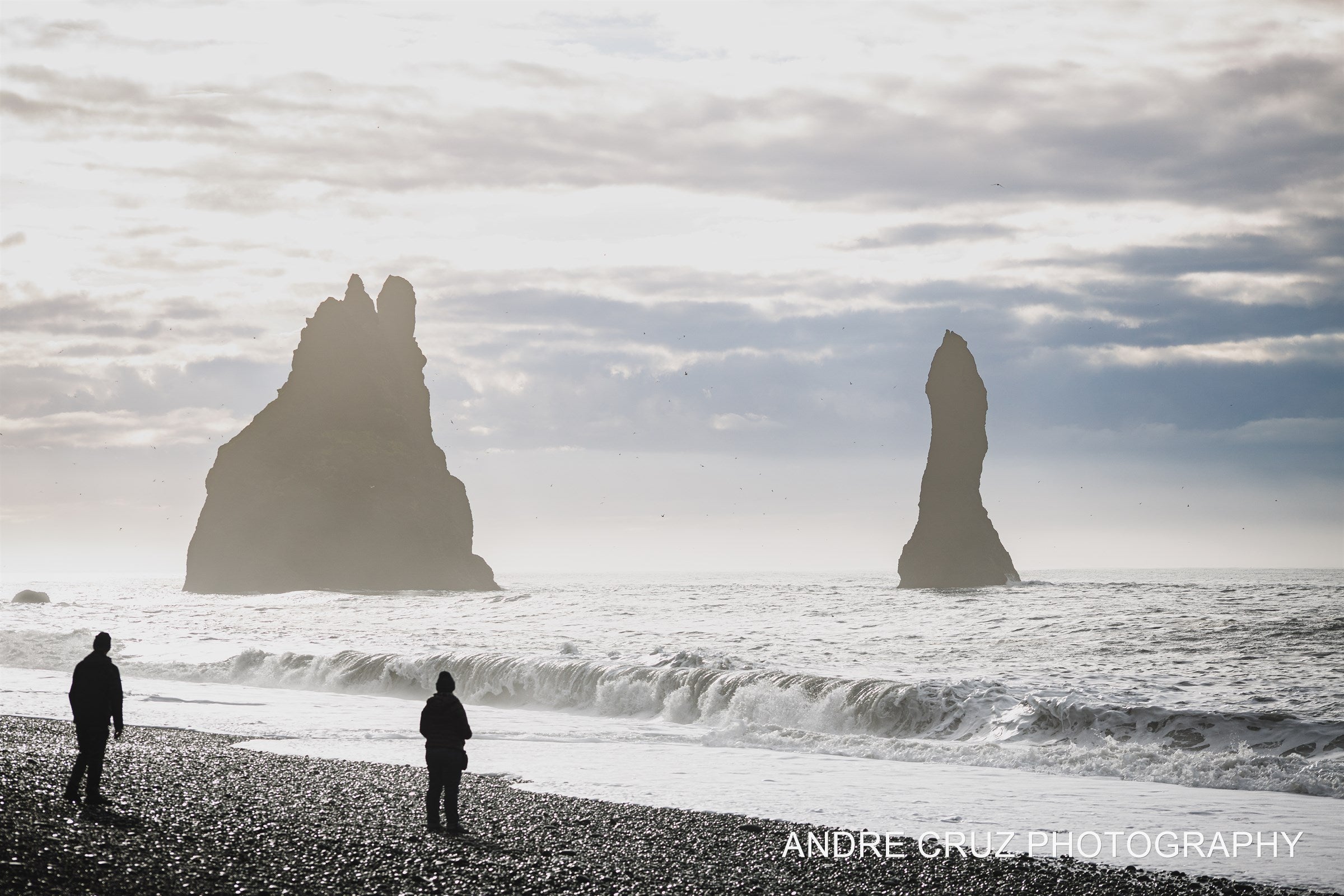 The Reynisdrangar sea stacks off a black sand beach with two figures for scale, Iceland