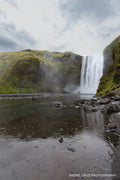 Skogafoss waterfall falling between moss-covered cliffs in southern Iceland, two figures small at its base