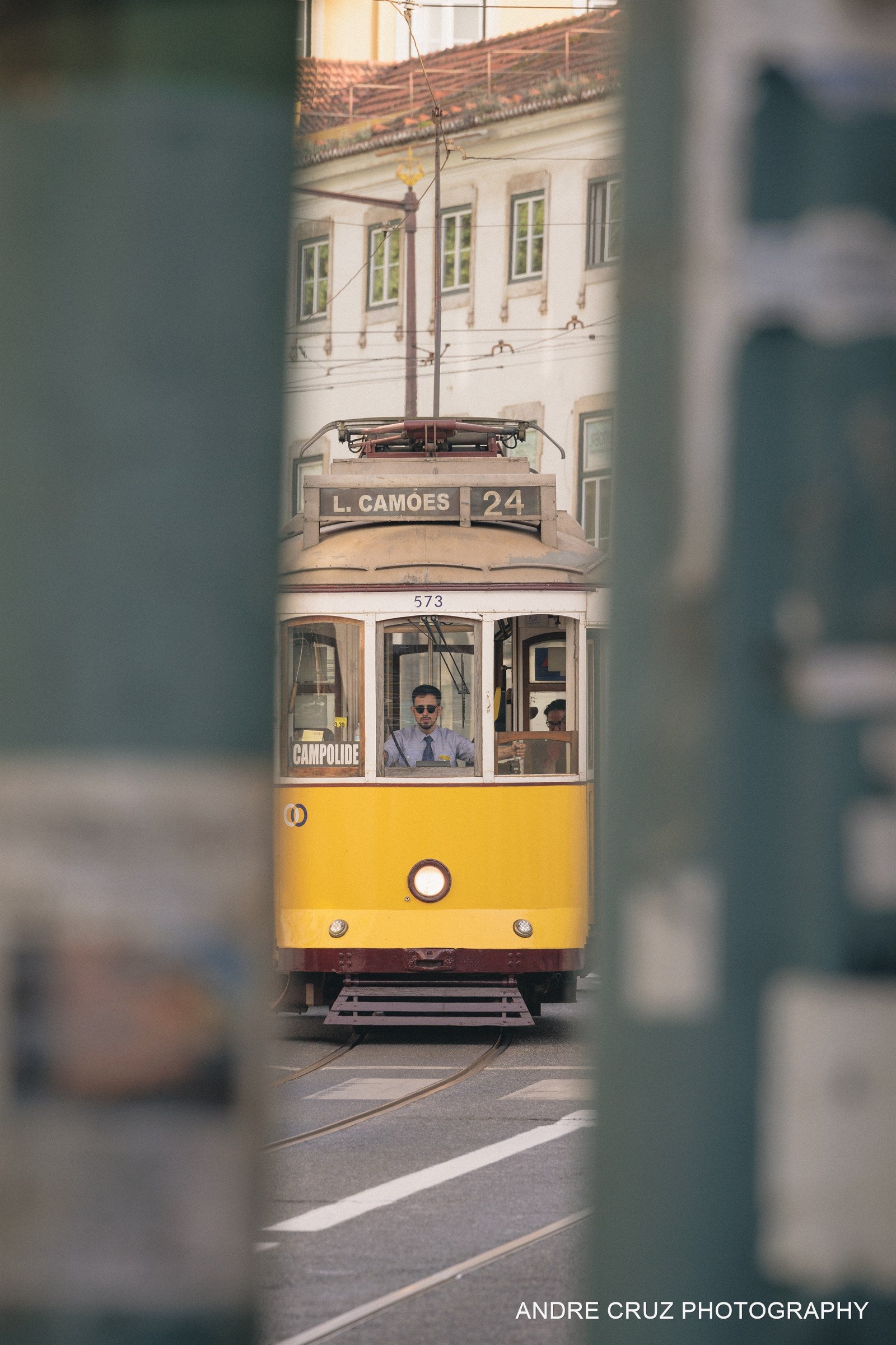 A yellow Lisbon tram seen between buildings on a narrow street, Portugal