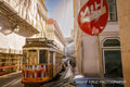 A yellow Lisbon tram beside a weathered red stop sign on a sunlit street, Portugal