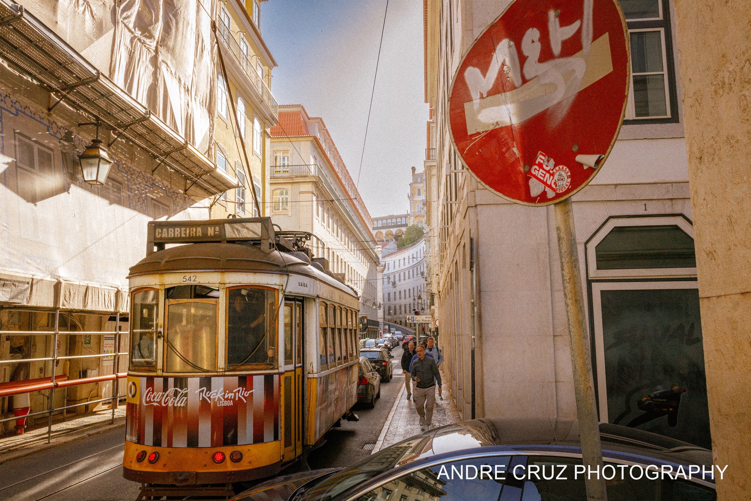 A yellow Lisbon tram beside a weathered red stop sign on a sunlit street, Portugal