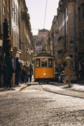 A yellow tram climbing a steep cobbled hill in Lisbon with pedestrians alongside, Portugal