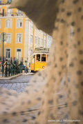 A yellow tram framed through a stone arch on a Lisbon street, Portugal