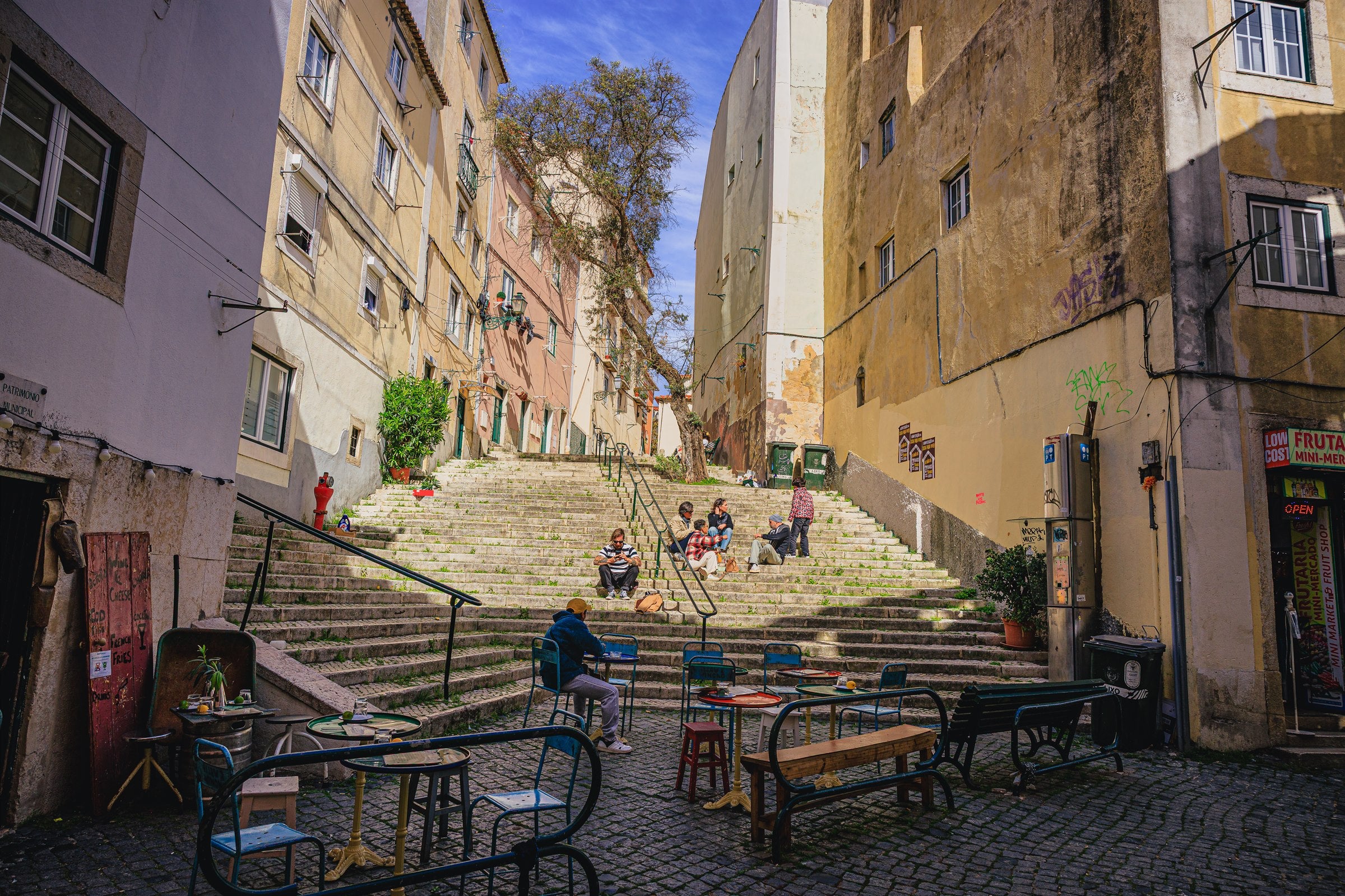 Stone staircase in the Alfama district of Lisbon with cafe tables and people sitting on the steps