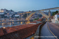 The lit Dom Luis I bridge at blue hour above the Calem cellar rooftops on the Douro, Porto