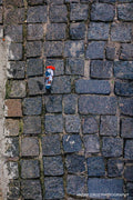 A child's sock with an orange cuff lying in the gap between grey granite cobblestones, seen from directly above