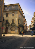 A tiled corner building on a steep Porto street with a lone walker carrying a yellow backpack